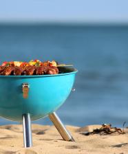 A grill with vegetables on top near a beach on the sand