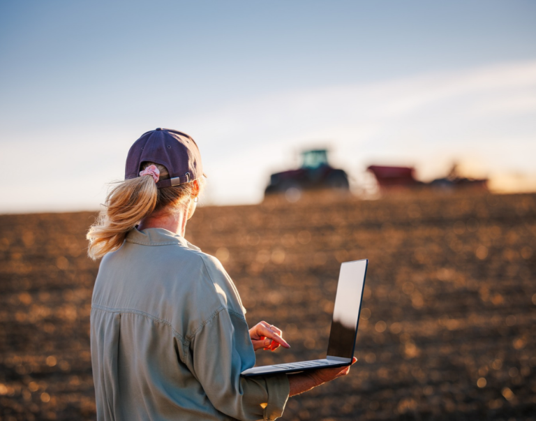 A farmer working on a laptop near a tractor