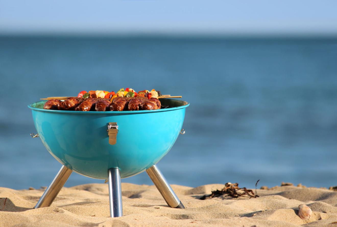 A grill with vegetables on top near a beach on the sand