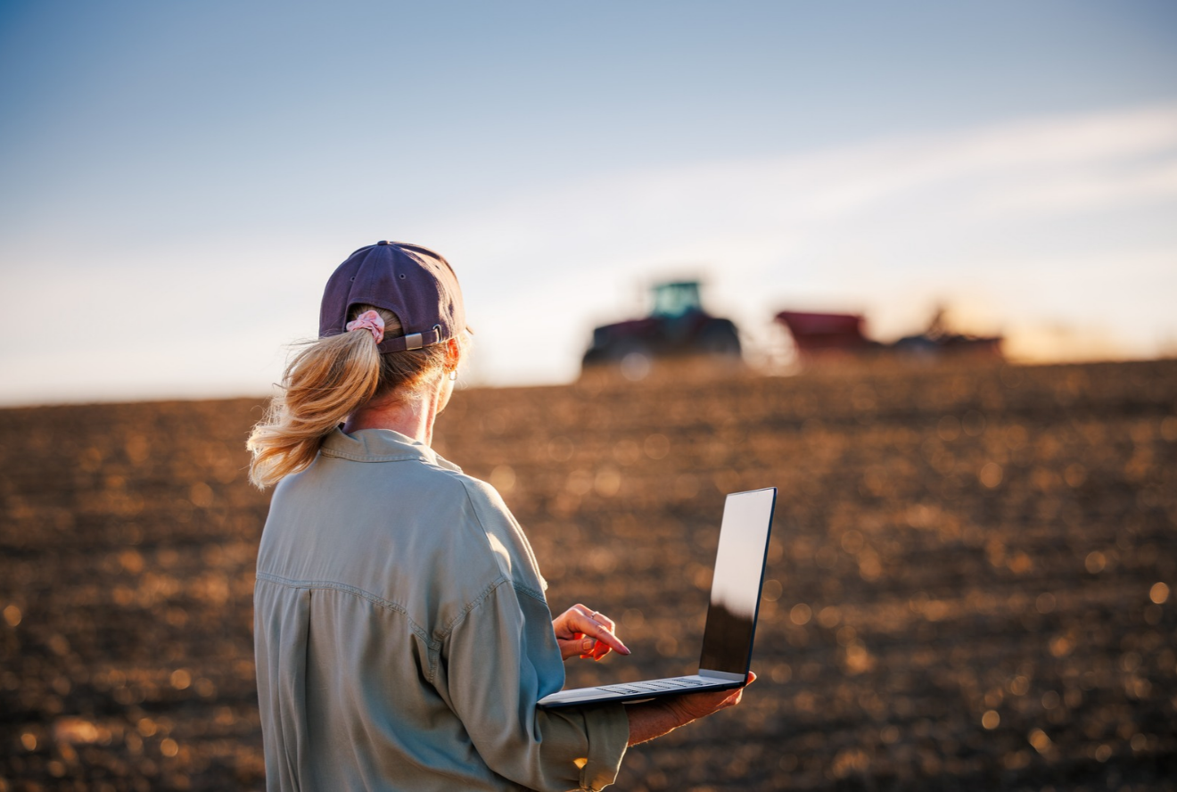 A farmer working on a laptop near a tractor